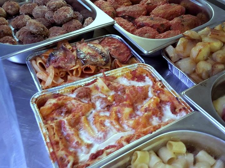Il banco della gastronomia con teglie di pasta al forno, polpette e patate