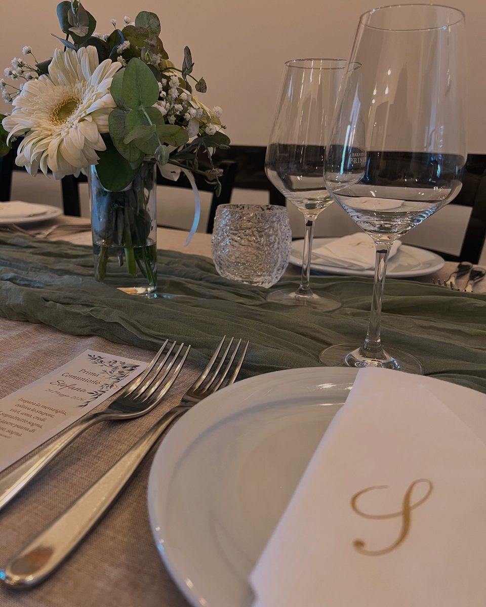 Un tavolo apparecchiato in sala, con fiori, calici e tovagliolo con la S